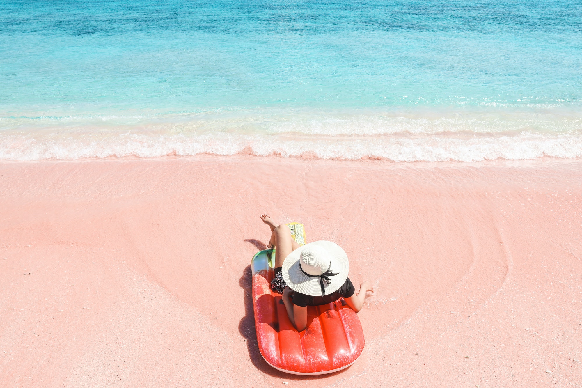 Woman laying on inflatable on pink sandy beach
